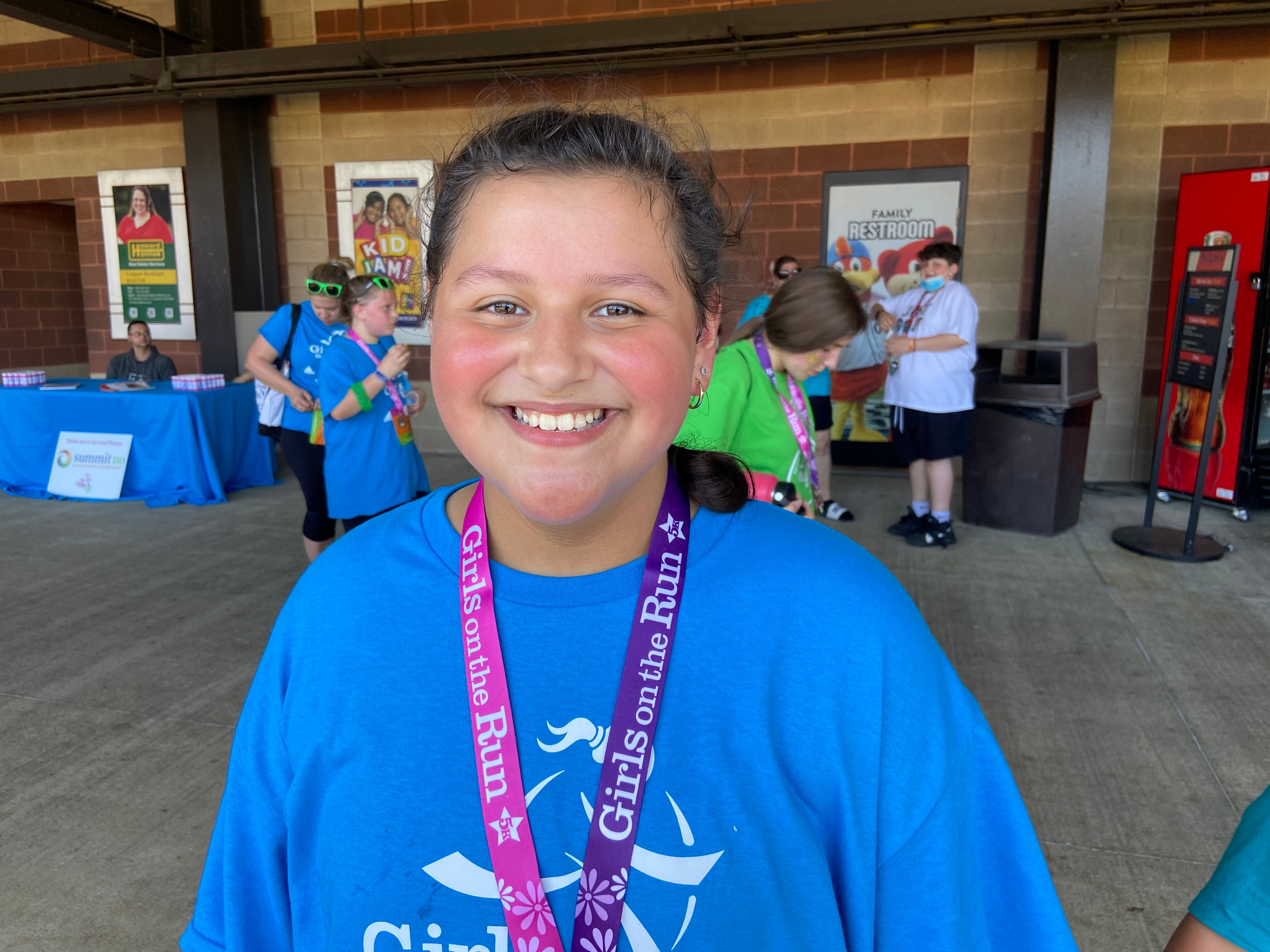 A Girls on the Run participant smiles wearing a blue shirt and her 5K medal