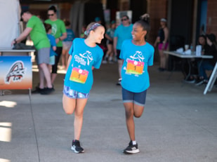 Two Girls on the Run participants wearing blue shirts stretch together