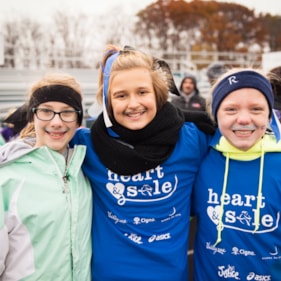 Three Heart & Sole participants smile with face paint on their faces and blue shirts at the 5K